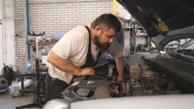 Profesyonel oto tamircisi arabanın kaputu altında çalışır. Tamirci atölyede veya serviste bir aracın motorunu tamir ediyor. Sakallı adam garajda otomobil motorunu kontrol ediyor. Bakım ve tanı kavramı.