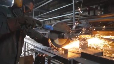 Atölyede çeliği kesen dairesel testereli sanayi işçisi. Güvenlik koruması altındaki adam metal kesmek için testere kullanıyor. Zanaatkar metali öğütüyor. Sıcak metalden kıvılcımlar çıkıyor. Yavaş çekim.