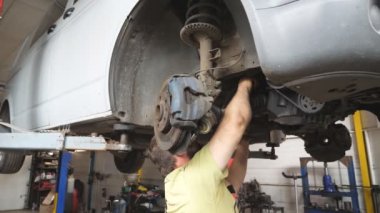 Otomatik serviste ingiliz anahtarı ile tanınmayan tamirci araba tamir ediyor. Garajdaki kaldırma aracının altında çalışan üniformalı profesyonel bir tamirci. Otomobil bakımı kavramı. Kapat..
