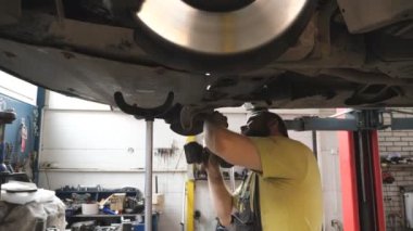 Profesyonel oto tamircisi atölyede özel elektrikli aletle cıvataları sıkılaştırıyor. Garajda kaldırma aracının altında çalışan bir adam. Sakallı tamirci araba tamir ediyor. Otomobil bakımı kavramı