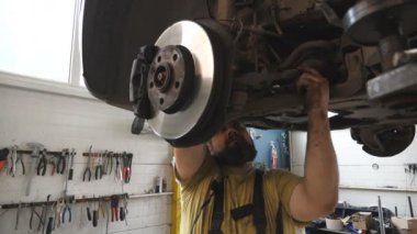 Sakallı tamirci atölyede ingiliz anahtarı ile araba tamir ediyor. Garajdaki bir kaldırma aracının altında çalışan profesyonel oto tamircisi. Otomobil bakımı kavramı. Yavaş çekim Dolly..
