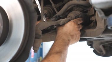 Kirli eller tamirci atölyede ingiliz anahtarı ile araba tamir ediyor. Garajda kaldırma aracının altında çalışan profesyonel oto tamircisi kolu. Otomobil bakımı kavramı. Yavaş çekim.