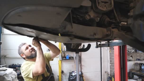 Brodaty Mechanik Instalujący Zabezpieczenie Silnika Samochodzie Pomocą Specjalnego Narzędzia Warsztacie — Wideo stockowe