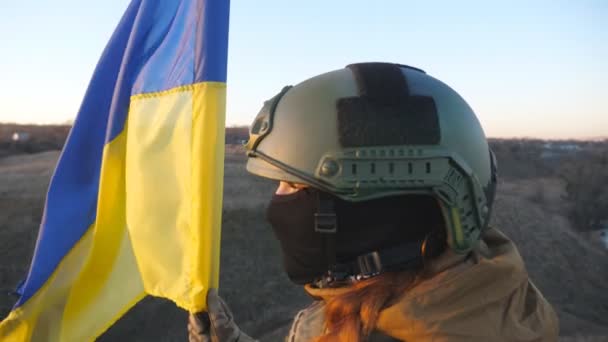 ウクライナ軍の女性は日没時に青黄色のバナーを振って丘のピークに立っている ウクライナの迷彩制服持ち上げフラグの若い女性兵士 ロシアの侵攻に対する抵抗 クレーンショット — ストック動画