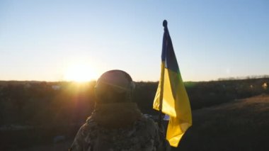 Dolly 'nin kadın asker çekimi Ukrayna bayrağını sallayarak tepenin zirvesinde duruyor. Kamuflaj üniformalı genç Ukraynalı asker gün batımında mavi-sarı pankart kaldırıyor. İstila direnişi kavramı.