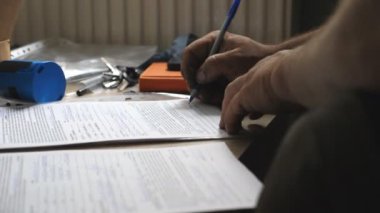 Kirli bir tamirci ya da tamirci elinde kalemle belgeye yeni bilgiler yazıyor. İşçinin erkek kolu masada yasal kağıtları imzalıyor. Sözleşmede imzası var. Not alıyorum. Yavaş çekim. Yakın çekim..