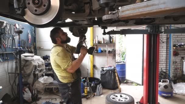 Automatyczny Mechanik Pracujący Pod Pojazdem Podnoszącym Garażu Profesjonalny Brodaty Mechanik — Wideo stockowe