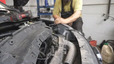 Tamirci oto servisinde araba bakımı yapıyor. Garajda kaputun altında çalışan profesyonel bir tamirci. Sakallı adam atölyede otomobili inceler. Nakil tanısı konsepti. Kapat.