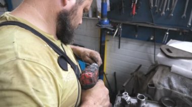 Tamirci, serviste elektrikli aletle otomatik bölümü tamir ediyor. Atölyeye yerleştirilmeden önce profesyonel bir tamirci detayları hazırlıyor. Garajda araba tamir eden bir adam var. Araç bakımı kavramı.
