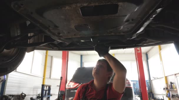 维修期间 汽车技工检查汽车底部 车间或车库在起重车下面工作的专业修理工 修理汽车的概念 慢动作 — 图库视频影像