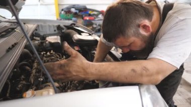 Tamirci arabanın motorunu tamir ediyor ve araba servisinde telefonla konuşuyor. Tamirci aracın kaputu altında çalışıyor ve iş arkadaşlarıyla görüşüyor. Otomobil motorunu kontrol et. Bakım ve tanı kavramı
