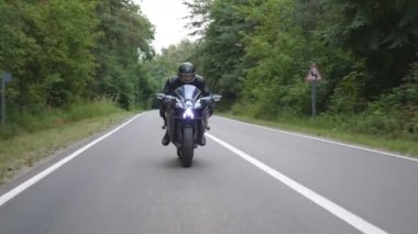 Kırsal Orman Yolu 'nda modern spor motosiklet süren kasklı genç bir adam. Motosikletli, tahta yolda motosikletiyle yarışıyor. Yolculuk sırasında bisiklet süren adam. Özgürlük ve macera kavramı. Ön görünüm.