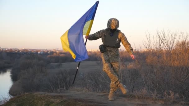 乌克兰军人带着蓝黄的旗帜在乡间的山丘上跳舞 身着迷彩服的快乐男兵庆祝乌克兰和俄罗斯战争的胜利 欧洲战争的结束 — 图库视频影像