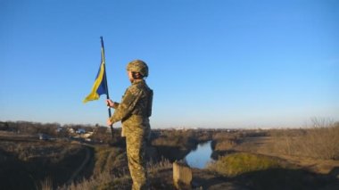 Askeri üniformalı asker portresi Ukrayna bayrağını kaldırdı. Elinde bayrak sallayan Ukraynalı asker. Rus saldırısına karşı zafer. İstila direnci konsepti. Yavaş çekim.