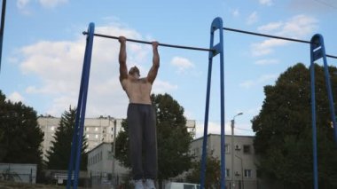 Spor alanında barfiks çeken kaslı bir sporcu. Genç sporcu çocuk parkında yatay barda egzersiz yapıyor. Güçlü sporcu adam dışarıda antrenman yapıyor. Sportif yaşam tarzı kavramı. Dolly vuruldu. Yaklaş..
