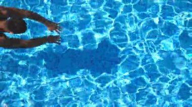 Havuza atlayan ve berrak su sıçratan gömlekli genç sporcu manzarası. Tanınmayan kaslı adam güneşli bir günde havuzda ferahlatıyor. Bronzlaşmış adam tatilde dinleniyor. Yavaş çekim
