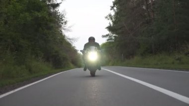 Kırsal Orman Yolu 'nda modern spor motosiklet süren kasklı genç bir adam. Motosikletli, tahta yolda motosikletiyle yarışıyor. Yolculuk sırasında bisiklet süren adam. Özgürlük ve macera kavramı. Ön görünüm.