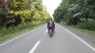 Motorcu, boş köy yolunda motorsikletle hızlanıyor. Orman yolunda, modern motorsikletle hızlı giden bir adam. Yolculuk sırasında bisiklet süren adam. Özgürlük ve macera kavramı. Hava görüntüsü.