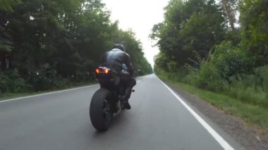 Orman yolunda motosiklet yarışı yapan bir motosikletli. Ormanın yakınındaki kırsal yolda kasklı bir adam spor motosikletine biniyor. Yolculuk sırasında bisiklet süren adam. Özgürlük ve macera kavramı. Hava görüntüsü.