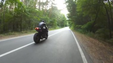 Orman yolundaki motosikletli motorcuları takip edin. Kasklı adam ormanın yakınındaki kırsal yolda modern spor motosiklet yarışı yapıyor. Yolculuk sırasında ya da yolculukta bisiklet süren adam. Özgürlük kavramı.