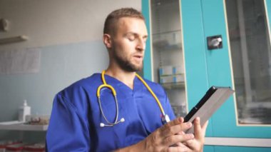 Genç doktor tablet kullanarak hastaya danışıyor. Dijital cihazı tutan ve biriyle konuşan bir tıp çalışanı. Corona salgını sırasında klinikte çalışan bir erkek doktor. Sağlık ve COVID-19 salgın konsepti