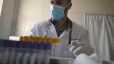 Doktor üniforma giyip test tüplerini kontrol ediyor. Doktor, COVID-19 'a analiz örnekleri inceliyor. Laboratuvarda çalışan bir bilim adamı. Korona virüsü salgınından korunmak için. Kapat..