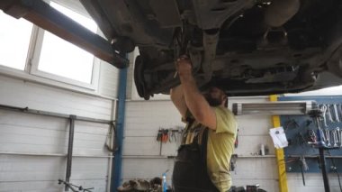 Tamirci araba tamirinde ingiliz anahtarıyla araba tamir ediyor. Garajdaki kaldırma aracının altında çalışan üniformalı profesyonel bir tamirci. Adam cıvata sıkıyor. Otomobil bakımı kavramı.