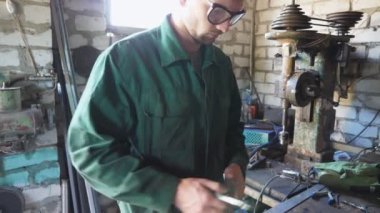 Üniformalı erkek tamirci atölyede metal işleriyle uğraşıyor. Garajda işini yapan koruyucu gözlüklü genç bir tamirci. Bakım hizmeti kavramı. Yavaşça kapat..