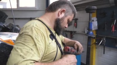 Tamirci, serviste elektrikli aletle otomatik bölümü tamir ediyor. Atölyeye yerleştirilmeden önce profesyonel bir tamirci detayları hazırlıyor. Garajda araba tamir eden bir adam var. Araç bakımı kavramı.