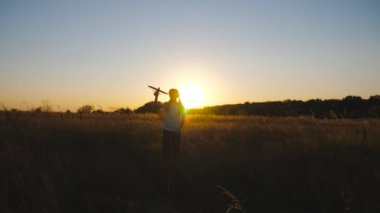 Küçük mutlu kız çim tarlasında uçakla yürüyor. Kaygısız çocuk gün batımında çayırların arasında oyuncak uçakla oynuyor. Küçük çocuk doğayla eğleniyor. Çocukluk hayali konsepti.