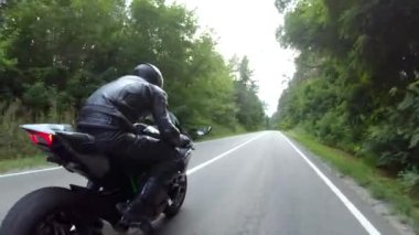 Orman yolundaki motosikletli motorcuları takip edin. Kasklı adam ormanın yakınındaki kırsal yolda modern spor motosiklet yarışı yapıyor. Yolculuk sırasında ya da yolculukta bisiklet süren adam. Özgürlük kavramı.