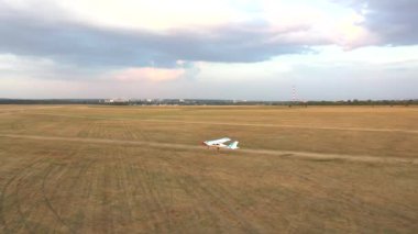 Küçük havaalanındaki çim pistinden küçük bir uçak kalkıyor. Hafif uçak kırsal pistte hareket ediyor ve uçuşa başlıyor. Ultra hafif spor uçak havaalanından ayrıldı. Havacılık konsepti. Hava görünümü