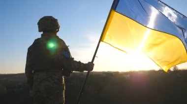 Ukrayna 'nın bayrağını günbatımına doğru sallayan Ukrayna ordusunun askeri. Askeri üniformalı ve miğferli adam bayrağı kaldırdı. Rus saldırısına karşı zafer. İstila direnişi kavramı.