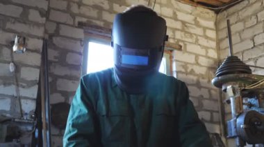 Mutlu genç tamirci işini bitirdikten sonra koruyucu maskeyi açar. İş kıyafetlerinde gülümseyen ve kameraya bakan kaynakçının portresi. Garajda çalışan sakallı bir tamirci. Düşük görünüm Yakın çekim.