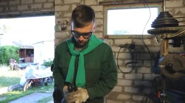Atölyede çalışırken koruyucu gözlüklü, komik dans eden mutlu bir tamirci. Üniformalı genç adam garajda eğleniyor ve eğleniyor. Neşeli tamirci iş yerinde aylaklık ediyor. Dolly vurdu..