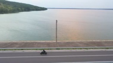 Göl kenarındaki otoyolda motosikletli bir adamın havadan çekilmiş fotoğrafı. Motosikletli büyük göletin yanında kır yolunda motosikletiyle yarışıyor. Yolculuk sırasında bisiklet süren adam. Özgürlük ve macera kavramı.