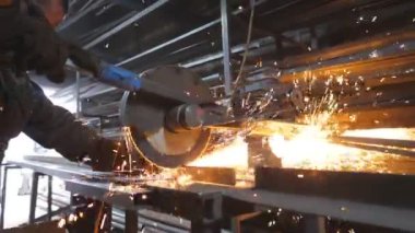 Atölyede çeliği kesen dairesel testereli sanayi işçisi. Güvenlik koruması altındaki adam metal kesmek için testere kullanıyor. Zanaatkar metali öğütüyor. Sıcak metalden kıvılcımlar çıkıyor. Yavaş çekim.