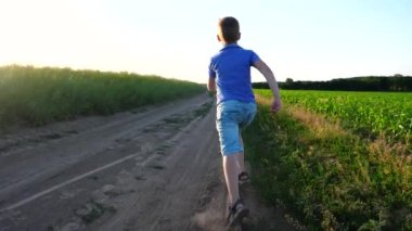 Yer yolunda koşan sandaletli, tanınmaz halde küçük bir çocuk toz izi bırakıyor. Kameralar, çayırlarda koşan ve mutlu bir yaz tatili geçiren mutlu çocuğu takip ediyor. Çocukluk ya da yaz konsepti. Yavaş çekim.