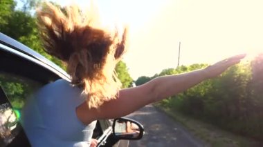Arabanın camından sarkan ve kırsal yolda giderken elini sallayan bir kadın. Otomotiv penceresinden bakan ve yaz doğasının tadını çıkaran bir kız. Seyahat konsepti. Yavaş çekim