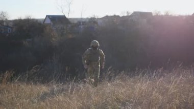 Üniformalı genç erkek asker kırsal kesimde kuru otların arasında koşuyor. Güneşli bir günde ekilmemiş çayırlarda koşan Ukraynalı asker. İstila direnişi. Rusya ve Ukrayna arasındaki savaş