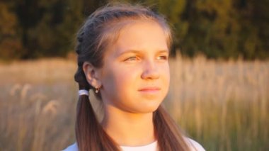 Güzel bir akşam gün batımına bakan ve parlak güneş ışınlarıyla aydınlanan küçük tatlı bir kızın portresi. Güzel bayan çocuk doğada vakit geçiriyor. Tasasız ve özgür olma kavramı. Dolly vurdu.