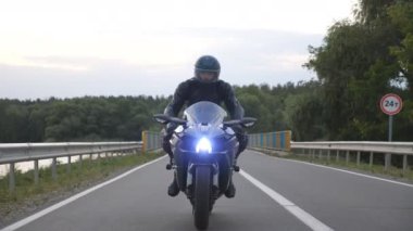 Motosikletli genç bir adam. Göl ya da nehir kenarındaki baraj yolunda bisiklet sürmek. Seyahat sırasında motosikletini kır yolunda süren bir motosikletçi. Seyahatte özgürlük ve macera kavramı. Kapat.
