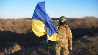 Ukrayna ordusunun kadın askeri doktoru kırsalda mavi-sarı pankartı kaldırıyor. Kamuflaj üniformalı genç bir kadın Ukrayna bayrağı sallıyor. Rus saldırısına karşı zafer. Savaşın sonu.