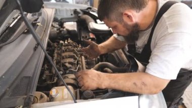 Tamirci arabanın motorunu tamir ediyor ve araba servisinde telefonla konuşuyor. Tamirci aracın kaputu altında çalışıyor ve iş arkadaşlarıyla görüşüyor. Otomobil motorunu kontrol et. Bakım ve tanı kavramı