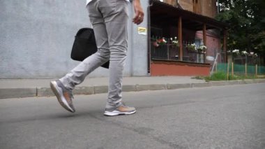 Sokak boyunca günlük giysiler giyen bir adamın bacakları. Elinde evrak çantasıyla iş merkezine giden kendinden emin iş adamının ayakları. İşe gidip gelen adamı takip et. Yavaş çekim. Yakın çekim..