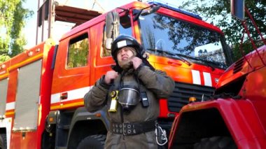 Genç itfaiyeci kaskını çıkartıyor ve kar maskesi itfaiye arabasının yanında duruyor. Erkek itfaiyeci yangından sonra ekipmanlarını çıkartıyor. İtfaiye, büyük kırmızı arabanın arka planında kameraya bakıyor..