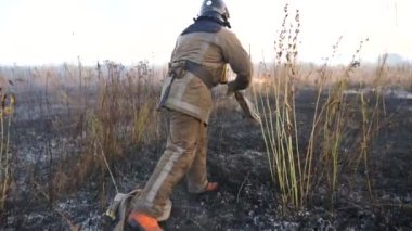 Tam teçhizatlı erkek itfaiyeci kırsal bölgedeki yangın hortumunu çözüyor. Üniformalı genç itfaiyeci çayırdaki kuru otları söndürmeye hazırlanıyor. Çevre sorunları ve küresel ısınma kavramı