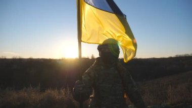 Ukrayna ordusunun kadın askeri sıhhiyesi sahada oturan ulusal bayrağı kaldırdı. Kamuflaj üniformalı genç bir kız gün batımına karşı Ukrayna bayrağı sallıyor. Rus saldırısına karşı zafer.