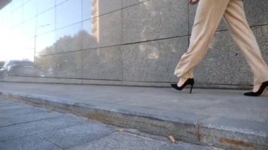 Modern binanın yakınında yürüyen iş kadınının ayakları. Yüksek topuklu ayakkabılı iş kadını bacakları şehir sokaklarında geziyor. Resmi giyimde başarılı bir bayan işe gidip geliyor. Kariyer anlayışı. Yavaş çekim.