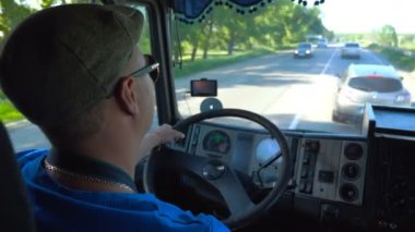 Tanınmayan kamyon şoförü güneşli bir günde ilçe yolunda gidiyor. Şapkalı adam ve güneş gözlüğü kamyonu dikkatli bir şekilde yolu izliyor. Kabinin içinden gelen trafiğin görünümü. İç çekim Yavaş mo Kapat
